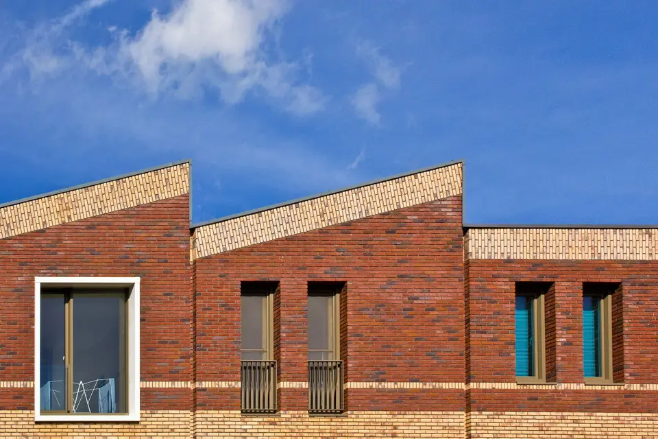 Een nieuwe gevel van rode baksteen met diepe, smalle ramen en schuine daklijnen tegen een blauwe lucht