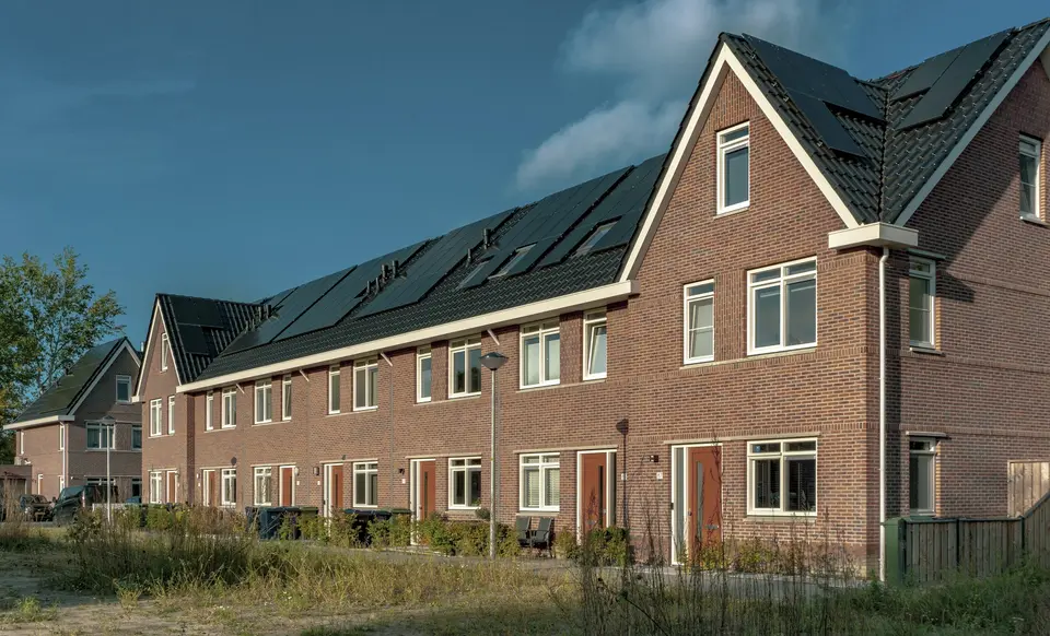 Een rij nieuwe bakstenen rijwoningen in Almere met zonnepanelen in de donkere daken, zonder schoorstenen